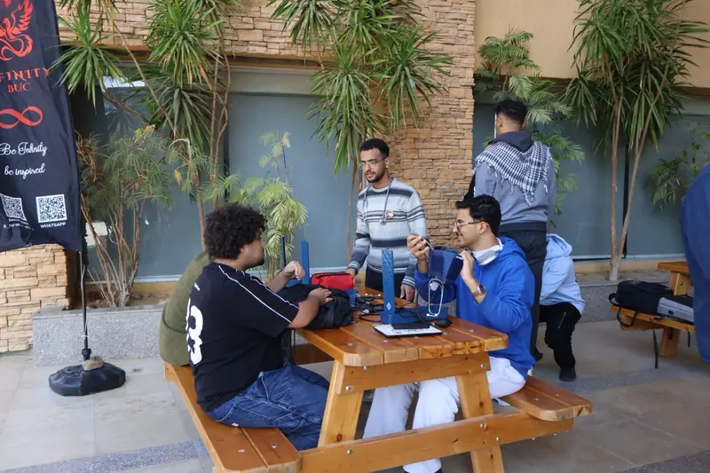 Students gather around a screening table outdoors, beside the Infinity team banner